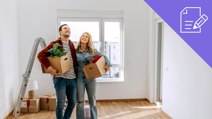 Casal segurando em caixas de mudanças numa sala vazia. Escadote e caixotes ao fundo.