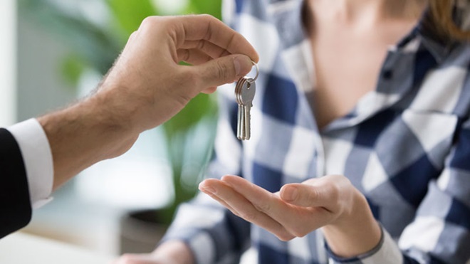 grande plano de uma mão de homem com fato a dar uma chave para a mão de uma mulher que veste uma camisa aos quadrados 