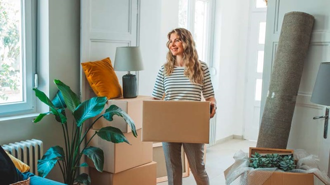 Mulher a entrar num apartamento alugado com caixas e elementos de decoração para a casa