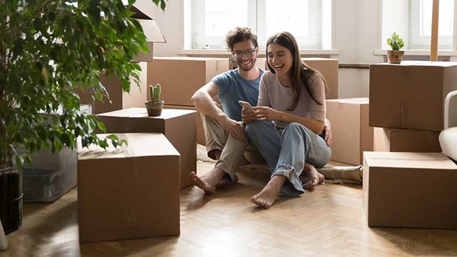 Casal sentado no chão redeado de caixas de mudança