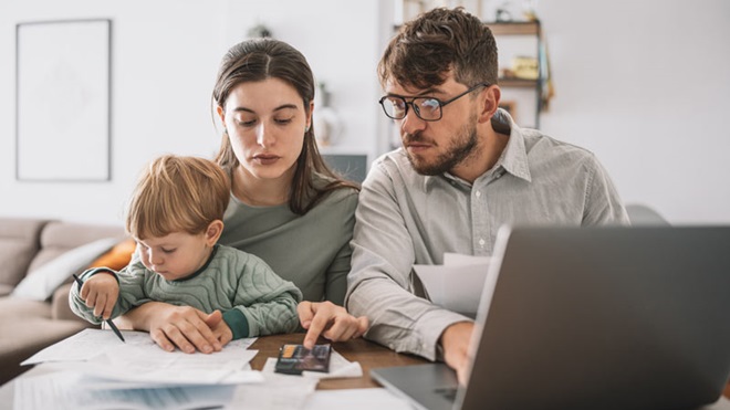 Pai, mãe e filho, com ar preocupado a fazerem contas com calculadora, portátil e a verem documentos