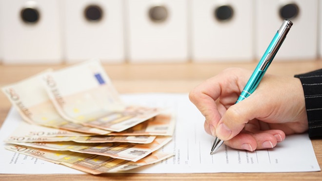 mão a escrever com uma caneta numa folha com notas em cima