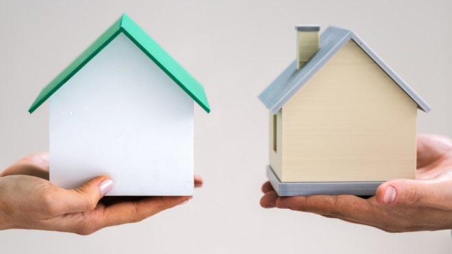 Duas mãos seguram duas casas de cartão, frente a frente