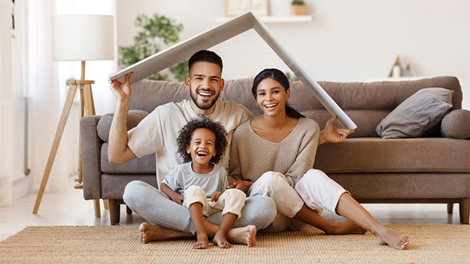 Família sentada no chão a segurar um cartão em forma de telhado