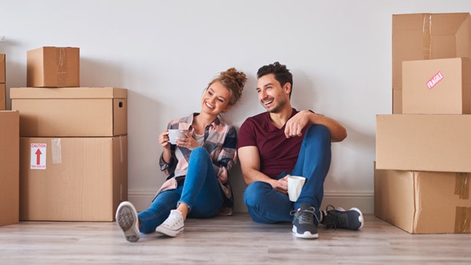 Casal jovem sentado numa casa nova ao lado de caixas por desempacotar