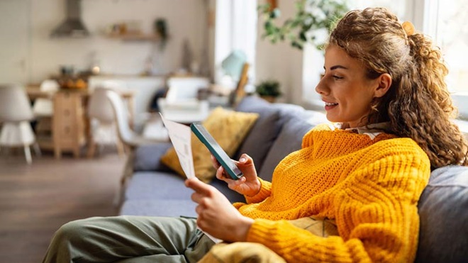 mulher no sofá a pagar conta com o telemóvel