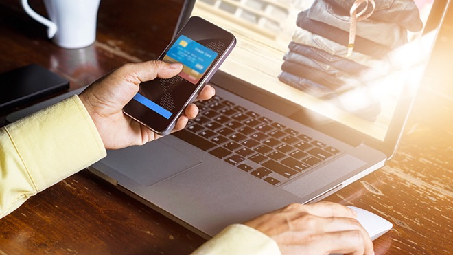 utilizador a usar smartphone e computador portátil para compras online