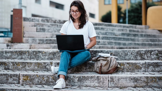 rapariga sentada numas escadas a escrever num computador portátil