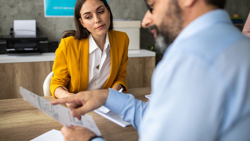 Homem a rever documentação com funcionária do banco