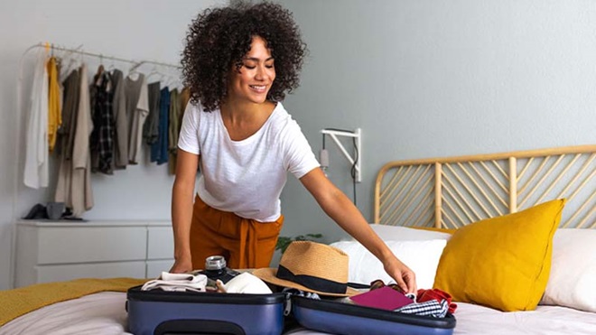 Mulher jovem ativa no quarto, em casa, faz a mala para um destino de férias