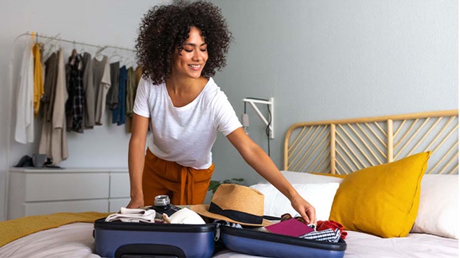 Mulher jovem ativa no quarto, em casa, faz a mala para um destino de férias