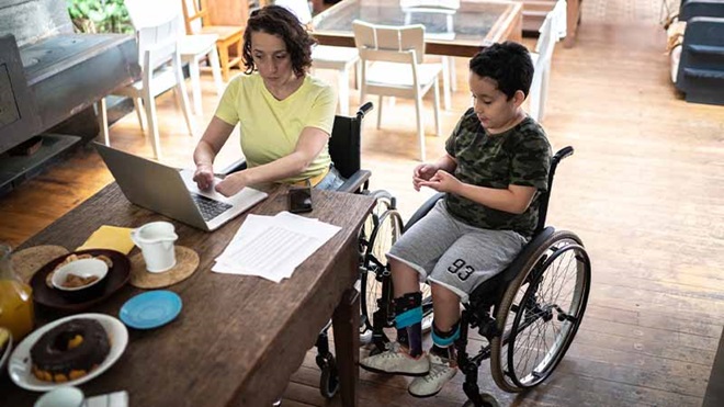 Mãe em teletrabalho com filho com deficiência motora em cadeira de rodas