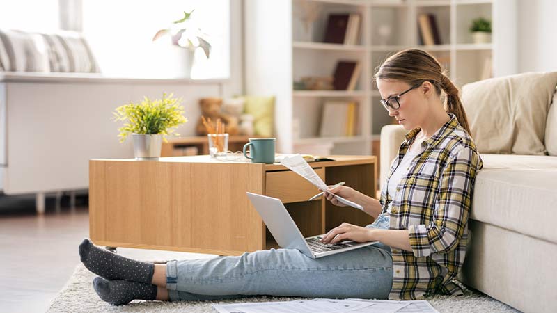 Mulher jovem sentada no chão da sala com um portátil no colo