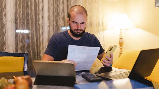 Homem a ler um papel com o telemóvel na mão