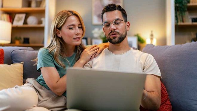 Casal sentado no sofá com portátil