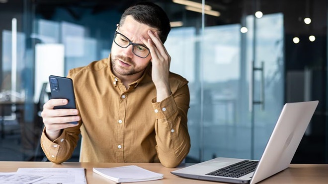 Mãos de pessoa a mexer num portátil, sobre uma mesa; ao lado está um sinal de alerta amarelo e preto