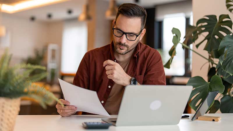 Homem no portátil a olhar para um papel