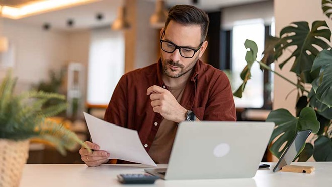Homem no portátil a olhar para um papel