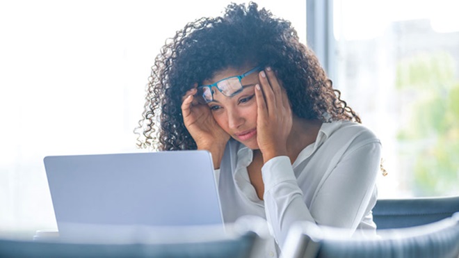 Mulher com ar desconsolado em frente ao ecrã de um portátil, sentada à secretária