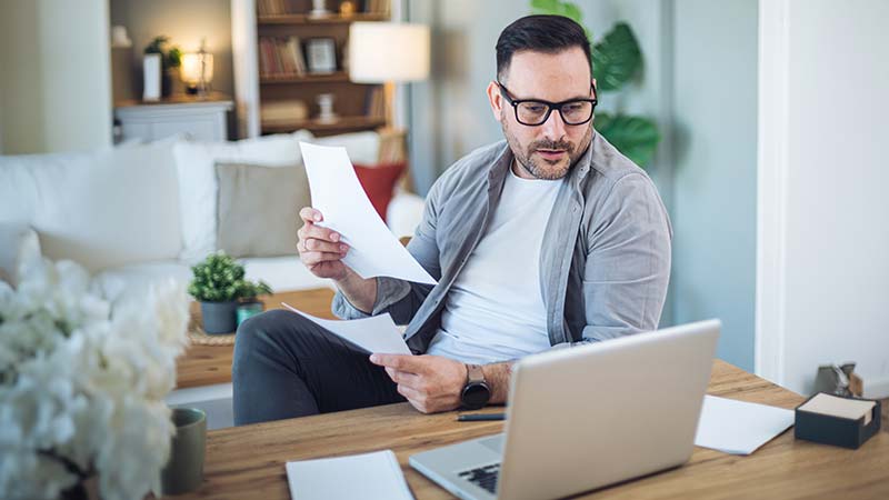 Homem com papéis a olhar para o portátil
