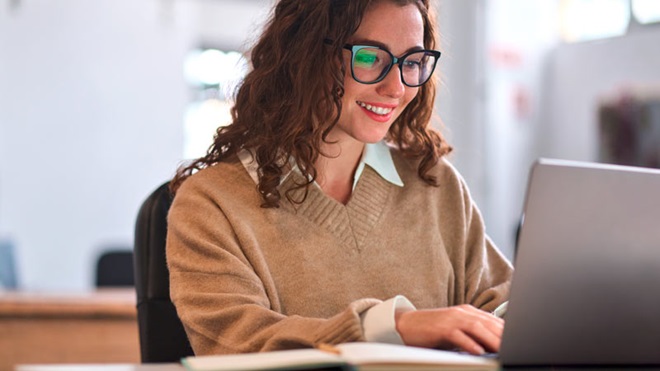Jovem na casa dos vinte anos, sentada numa secretária preenhe um documento no computador