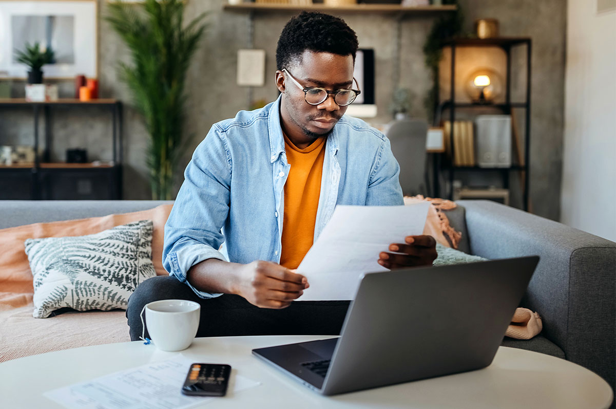 Homem a olhar para um papel junto ao portátil com a calculadora aberta no telemóvel