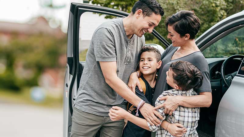 Casal com dois filhos abraçados junto ao carro, na rua