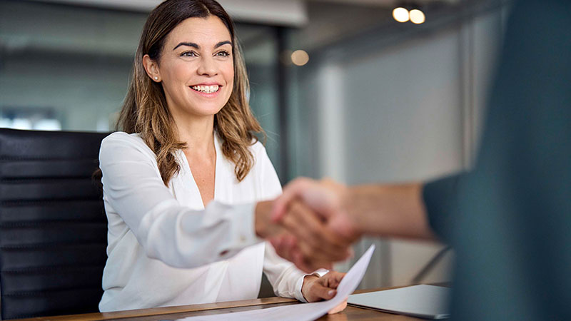 Mulher jovem sentada à secretária a apertar a mão a cliente 
