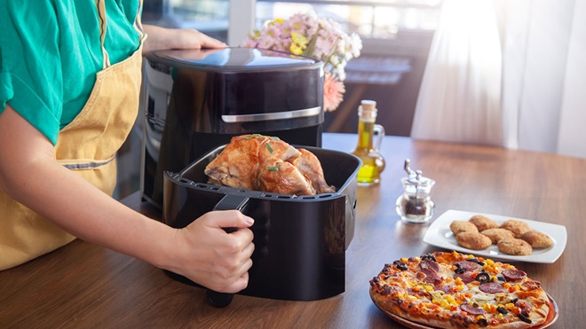Pessoa de avental a abrir a gaveta de uma air fryer grande com um frango inteiro já assado