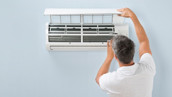 Homem a abrir um aparelho de ar condicionado que está numa parede