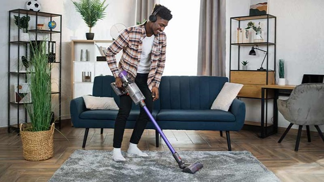 Homem jovem a aspirar o tapete da sala com um aspirador vertical sem fios