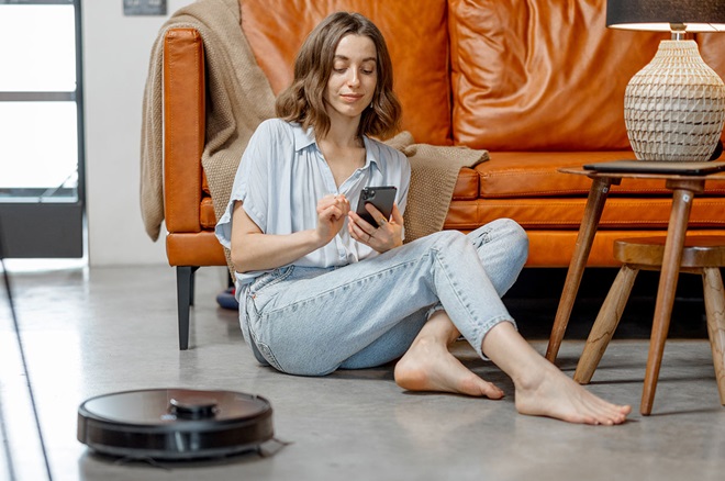 Rapariga com telemóvel e aspirador robô