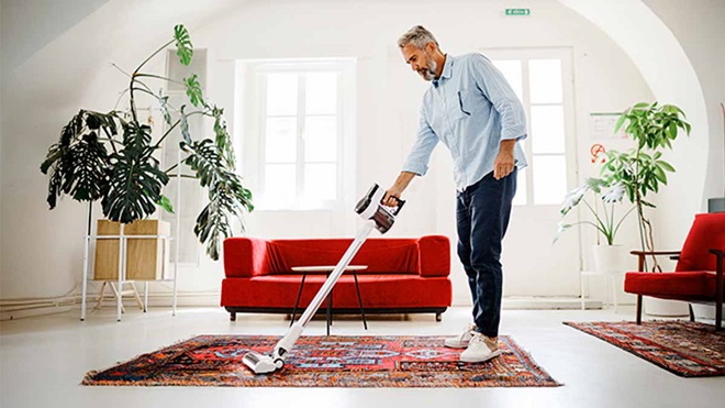 Homem aspira a casa com um aspirador vertical sem fios