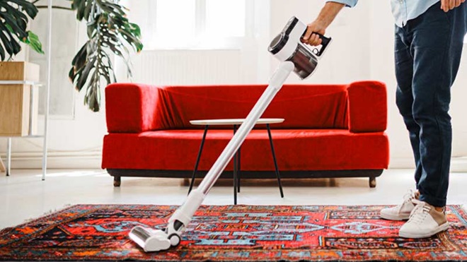 Homem a aspirar tapete numa sala com um aspirador vertical sem fio
