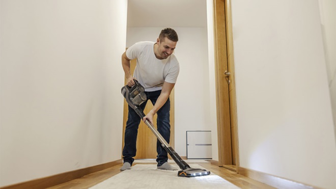 Homem a aspirar uma passadeira num corredor com um modelo vertical sem fio