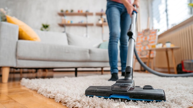 Uma pessoa aspira uma carpete branca sobre chão de parquet numa sala de estar com sofá branco