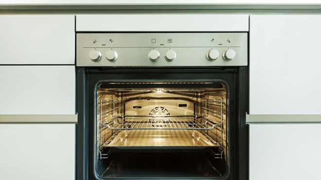 Forno com a luz acessa, encastrado numa cozinha branca