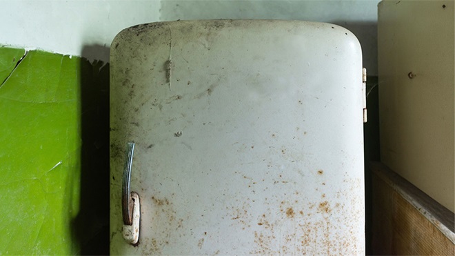 Frigorífico antigo com ferrugem encostado a parede verde