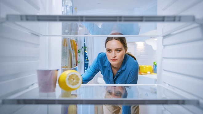 Mulher com ar sério inspeciona o seu frigorífico vazio