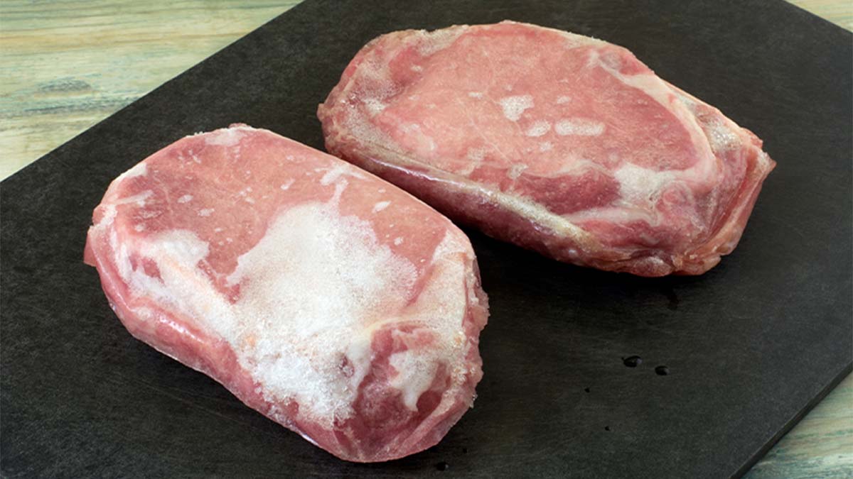 Carne de porco em cima de tábua preta com pedaços de gelo à superfície