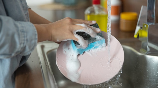 Senhora a lavar um prato no lava-loiça e com água a correr