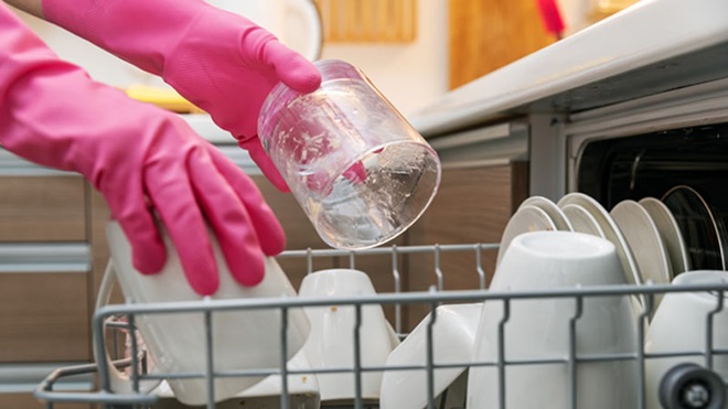 Mãos com luvas de borracha cor de rosa a pôr um copo dentro da máquina de lavar loiça 
