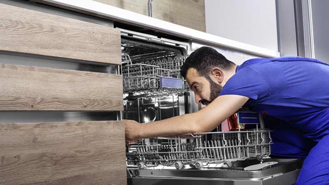 Um homem vestido de azul manipula uma máquina de lavar loiça.