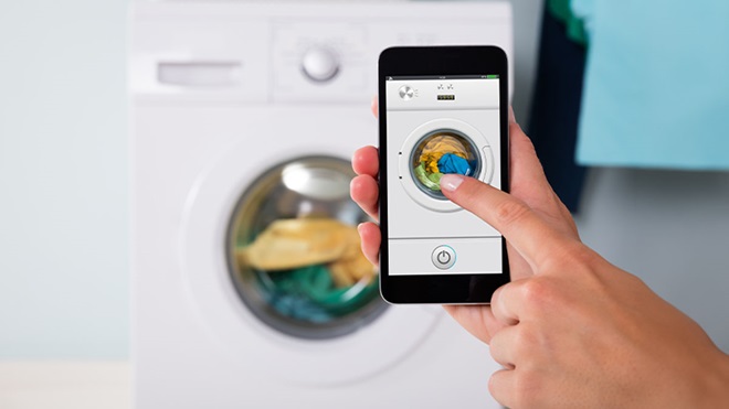 Pessoa a segurar smartphone em frente a máquina de lavar roupa inteligente