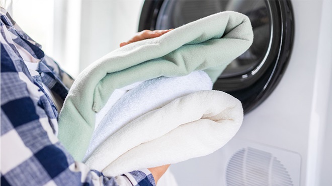 pessoa a segurar roupa lavada e dobrada em frente a máquina de secar roupa