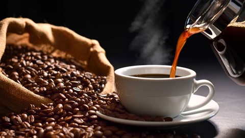 saco de serrapilheira com grãos de café do lado esquerdo; bule a deitar café numa chávena branca do lado direito