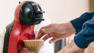 Homem a tirar chávena com meia de leite de uma máquina de café.