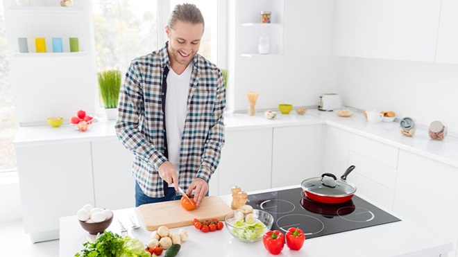 Homem a cortar legumes numa tábua para cozinhar numa placa de indução 