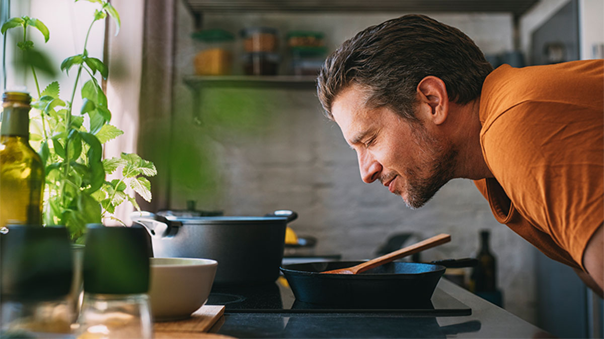 Homem a sentir o aroma do cozinhado numa placa de indução. Cozinha moderna