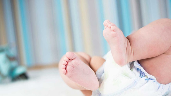 Plano aproximado da parte inferior do corpo de um bebé, onde se vê em destaque os pés e as pernas rechonchudas, dobradas, e parte da fralda que o bebé está a utilizar.